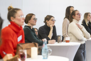 Ein kleine Gruppe Teilnehmerinnen an Stehtischen, die Frau Buschhoffs Vortrag interessiert zuhört.